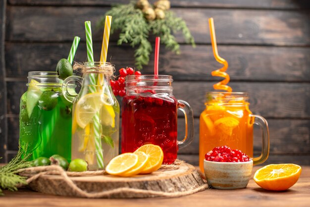 Vista frontal cercana de jugos frescos orgánicos en botellas servidas con tubos y frutas sobre una tabla de cortar de madera sobre una mesa marrón