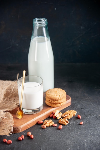 Vista frontal cercana de una leche fresca en un vaso y botella de galletas sobre tabla de madera color nude toalla nueces cacahuetes sobre superficie oscura