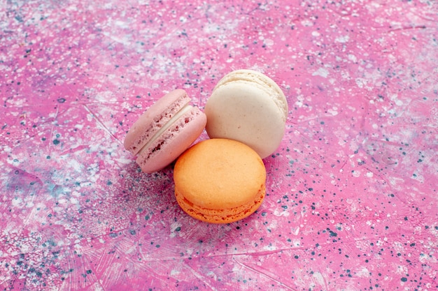 Vista frontal cercana macarons franceses deliciosos pasteles en el escritorio rosa