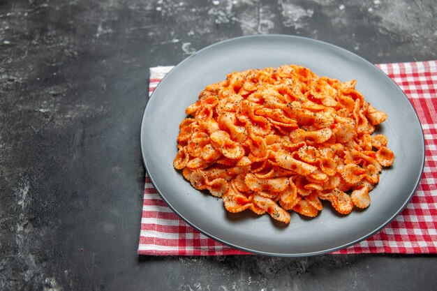 Vista frontal cercana de pasta fácil para cenar en una placa negra sobre una toalla despojada de rojo