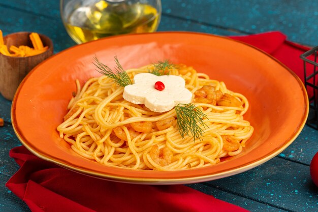 Vista frontal cercana pasta italiana cocida con verduras dentro de un plato naranja con aceite y verduras en azul