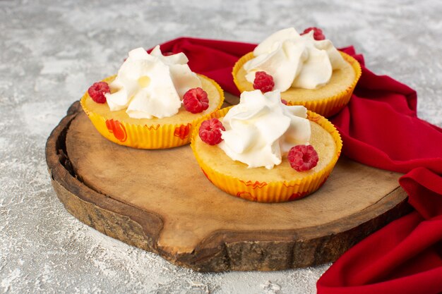 Vista frontal cercana pasteles con crema deliciosa horneada diseñada con frambuesas en la superficie gris