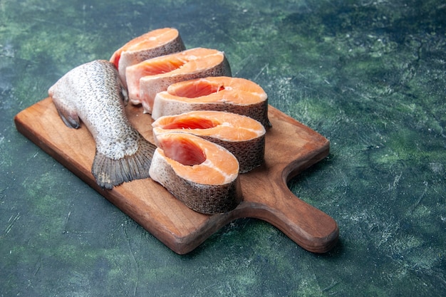 Foto gratuita vista frontal cercana de pescados crudos frescos en la tabla de cortar de madera marrón en la mesa de colores mezclados oscuros con espacio libre