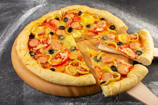 Vista frontal cercana pizza cursi con tomates rojos, aceitunas negras, pimientos y salchichas en el oscuro escritorio