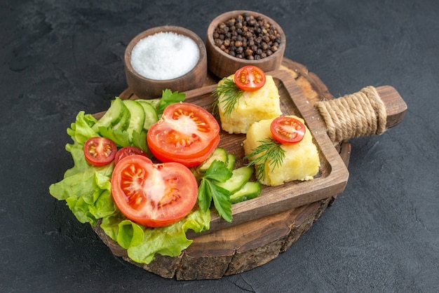 Vista frontal cercana de queso de verduras frescas picadas y enteras en la tabla de cortar y especias sobre superficie negra