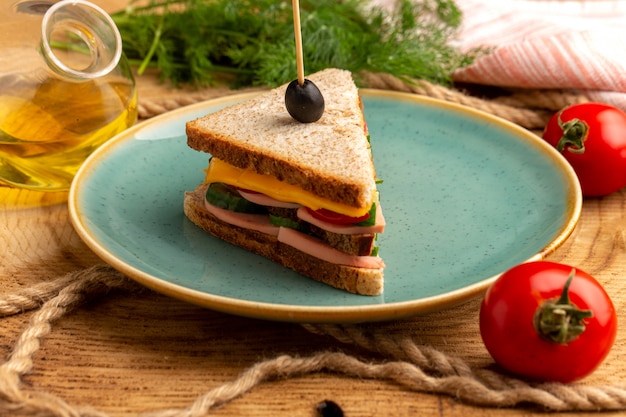 Vista frontal cercana sabroso sándwich con aceitunas, jamón y tomates dentro de la placa junto con cuerdas
