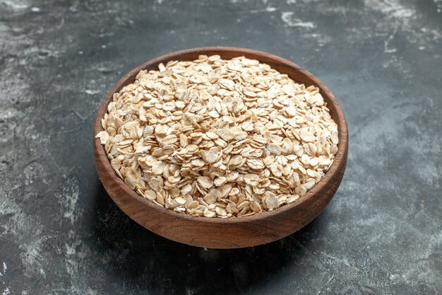 Vista frontal cercana de salvado de avena orgánico en una olla de madera marrón sobre fondo oscuro