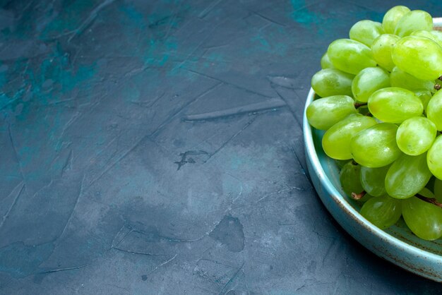 Foto gratuita vista frontal cercana uvas verdes frescas frutas suaves y jugosas dentro de la placa en el escritorio azul oscuro.