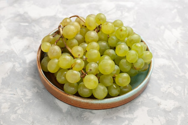 Vista frontal cercana uvas verdes frescas jugosas frutas dulces suaves en el escritorio blanco fruta fresca jugo suave vino