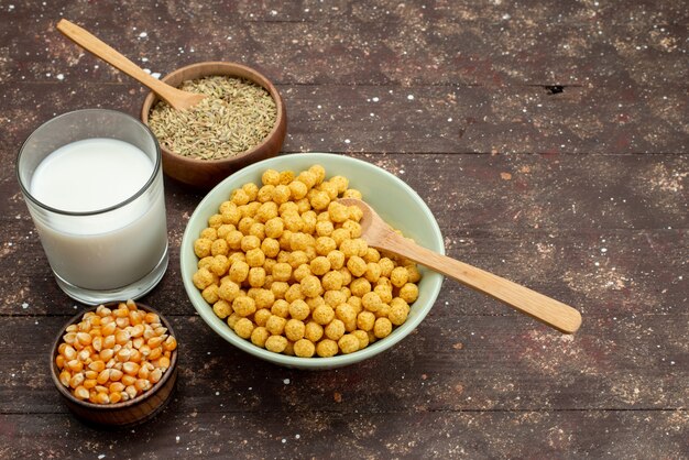 Vista frontal de cereales amarillos dentro de la placa con leche fría fresca sobre madera oscura, cereales para el desayuno cereales comida