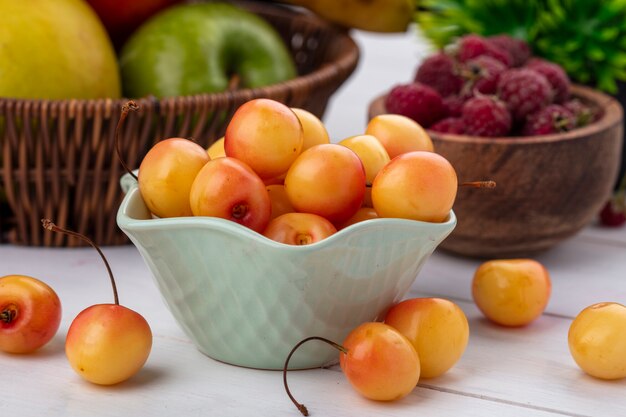 Vista frontal de cerezas blancas en un recipiente con frambuesas sobre una superficie blanca