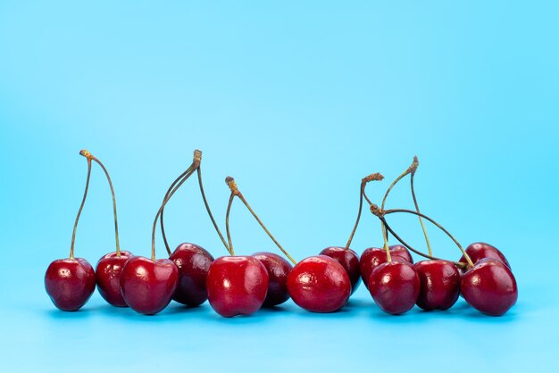 Una vista frontal de las cerezas rojas frescas suaves y ácidas en azul, color de verano de frutas