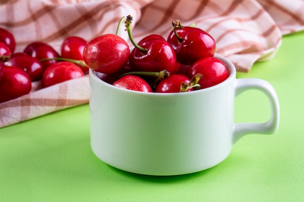 Vista frontal de cerezas en una taza con una toalla de cocina en verde claro