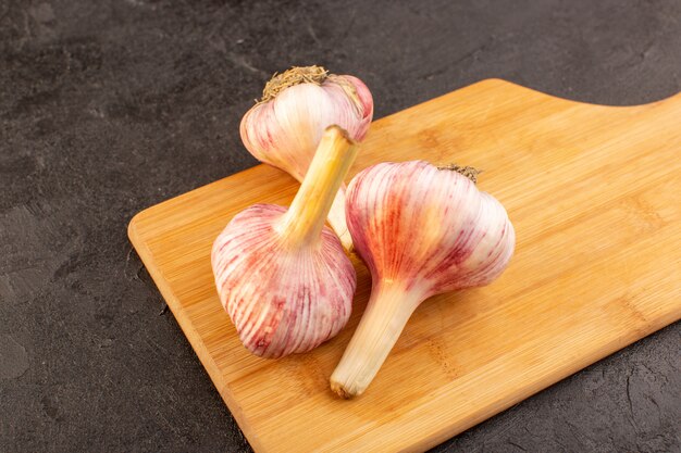 Una vista frontal cerrada de ajos enteros maduros frescos aislados en el escritorio de madera marrón y fondo gris ingrediente vegetal comida comida