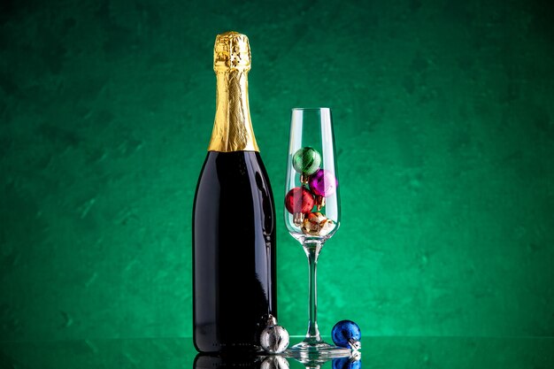 Vista frontal champagne pequeñas bolas de Navidad en copa de vino sobre superficie verde