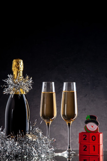 Foto gratuita vista frontal de champán en botellas y vasos de bloques de madera sobre una superficie oscura