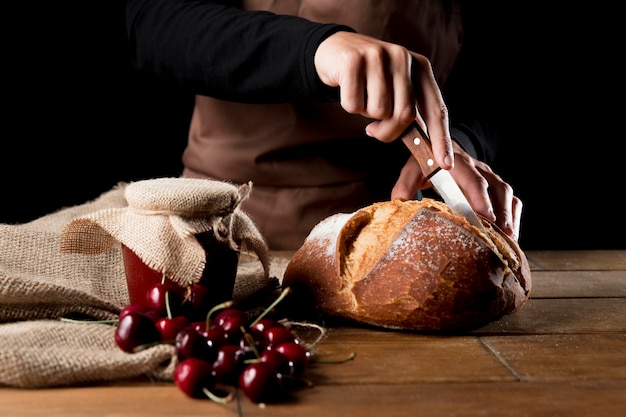 Vista frontal del chef cortando pan con tarro de mermelada de cerezas