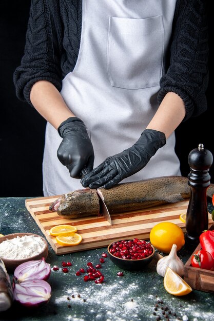 Vista frontal del chef cortar la cabeza de pescado en una tabla de cortar, molinillo de pimienta, tazón de harina, semillas de granada en un tazón en la mesa de la cocina