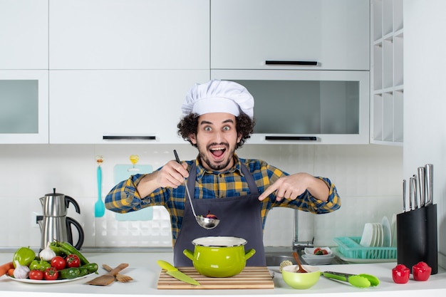 Foto gratuita vista frontal del chef con degustación de verduras frescas y señalando comida preparada en la cocina blanca