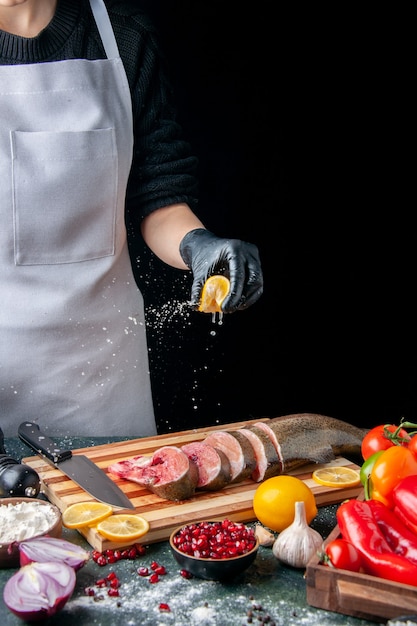 Foto gratuita vista frontal del chef exprimiendo limón en rebanadas de pescado cuchillo en tabla de cortar verduras en tabla de servir de madera en la mesa de la cocina