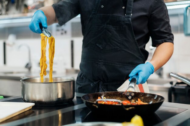 Vista frontal del chef con guantes cocinando pasta en la cocina