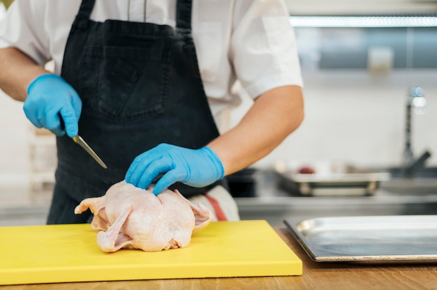 Foto gratuita vista frontal del chef con guantes cortando pollo