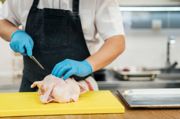 Vista frontal del chef con guantes cortando pollo