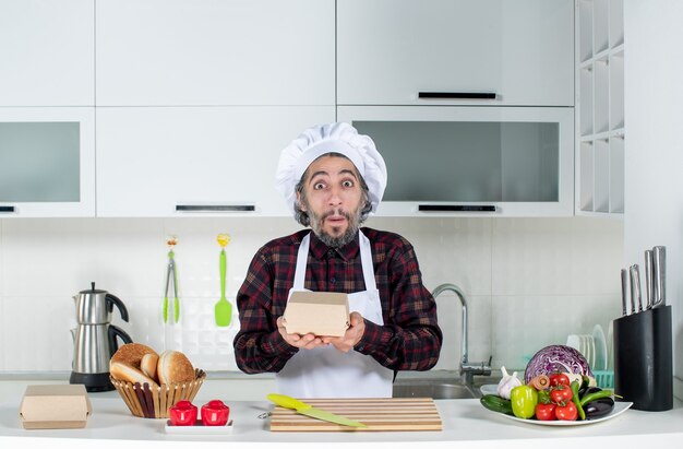 Vista frontal del chef masculino en caja de sujeción uniforme en la cocina moderna