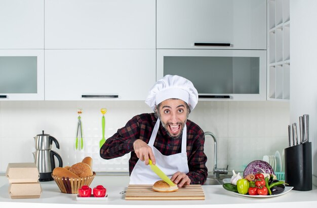 Vista frontal del chef masculino cortando pan sobre tablero de madera en la cocina