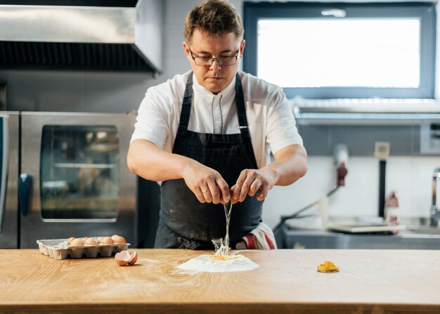 Vista frontal del chef masculino rompiendo el huevo sobre la harina para crear masa
