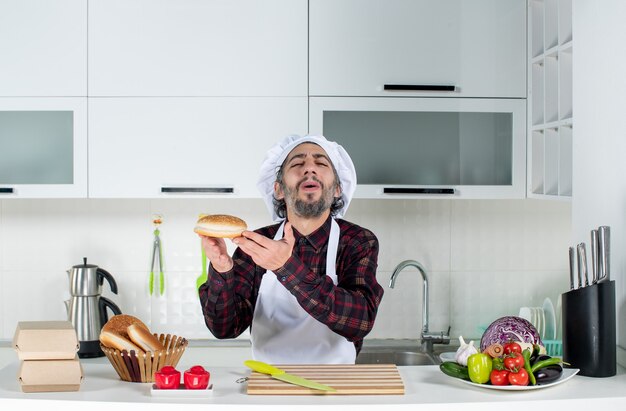 Vista frontal del chef masculino satisfecho sosteniendo pan en la cocina moderna