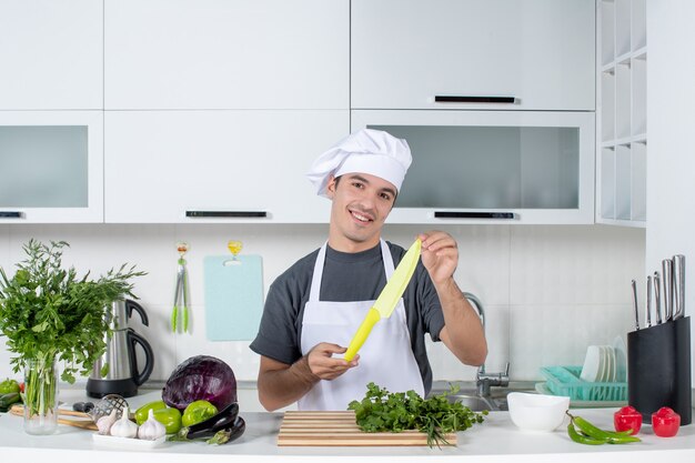 Vista frontal chef masculino satisfecho en uniforme sosteniendo un cuchillo en la cocina