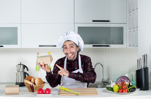 Vista frontal del chef masculino sonriente apuntando a la caja de hamburguesas en la cocina