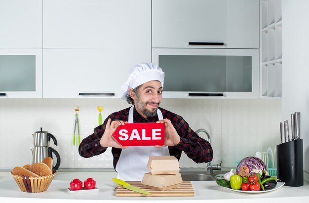 Vista frontal del chef masculino sonriente sosteniendo cartel de venta en la cocina