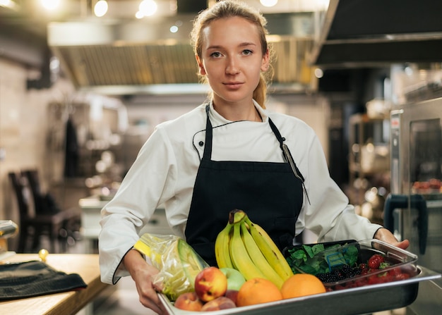 Vista frontal de la chef mujer sosteniendo una bandeja de fruta