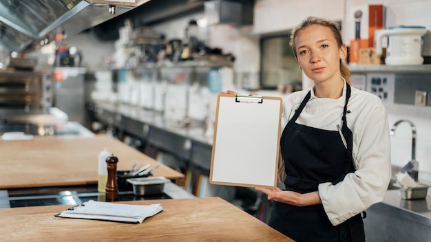 Vista frontal de la chef mujer sosteniendo el portapapeles en la cocina