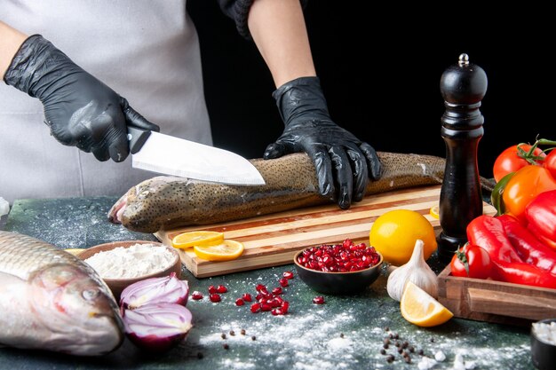 Vista frontal del chef picar pescado crudo en tablero de madera molinillo de pimienta tazón de harina semillas de granada en un tazón en la mesa de la cocina