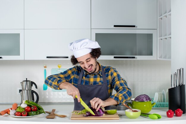 Foto gratuita vista frontal del chef sonriente y feliz con verduras frescas para picar alimentos en la cocina blanca