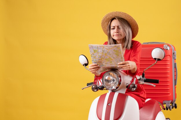 Vista frontal de la chica guapa ocupada en ciclomotor con maleta roja mirando el mapa