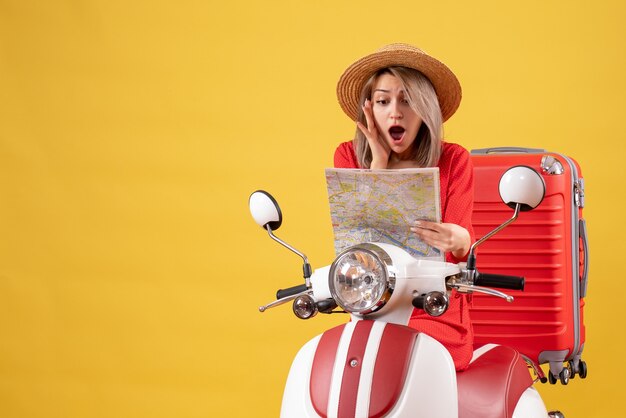 Vista frontal de la chica guapa sorprendida en ciclomotor con maleta roja con mapa