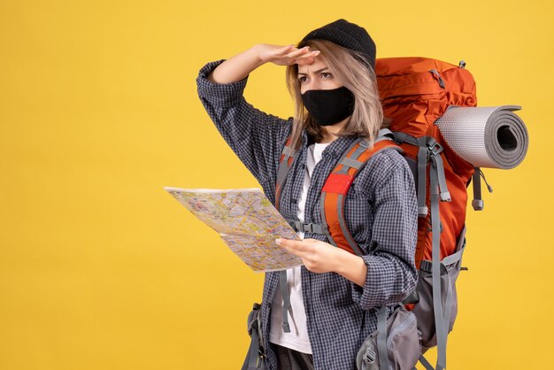 Vista frontal de la chica guay viajera con máscara negra y mochila con mapa mirando algo