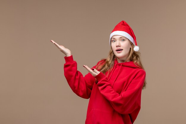 Vista frontal chica de Navidad con cara de sorpresa sobre fondo marrón mujer vacaciones emoción de Navidad