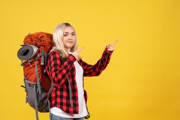 Vista frontal chica rubia con su mochila apuntando a algo