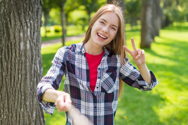 Vista frontal chica rubia tomando una selfie junto a un árbol