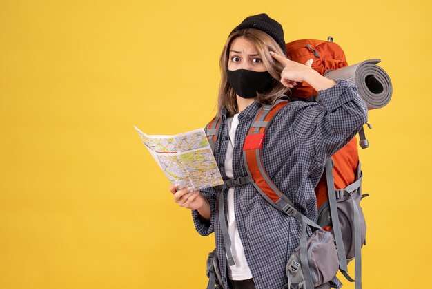 Vista frontal de la chica viajera confundida con máscara negra y mochila con mapa