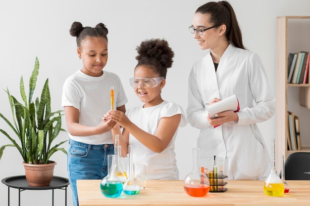 Vista frontal de chicas disfrutando de un experimento de química con una mujer científica