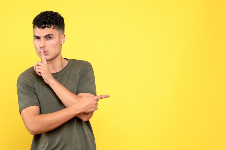 Foto gratuito vista frontal de un chico el chico se lleva un dedo a los labios y mira hacia adelante