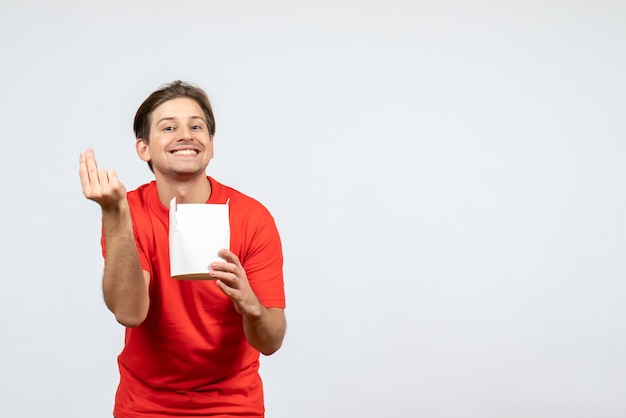 Vista frontal del chico joven feliz en blusa roja con caja de papel sobre fondo blanco.