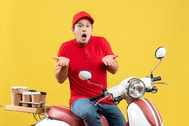 Vista frontal del chico joven preguntándose con blusa roja entregando pedidos sobre fondo amarillo