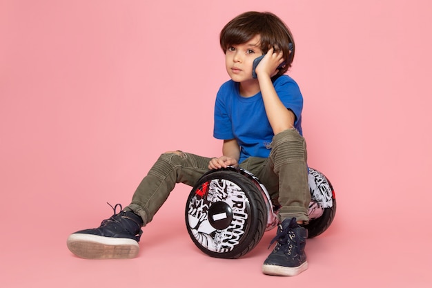 Foto gratuita una vista frontal chico lindo en camiseta azul y pantalón caqui hablando por teléfono montando en segway en el piso rosa